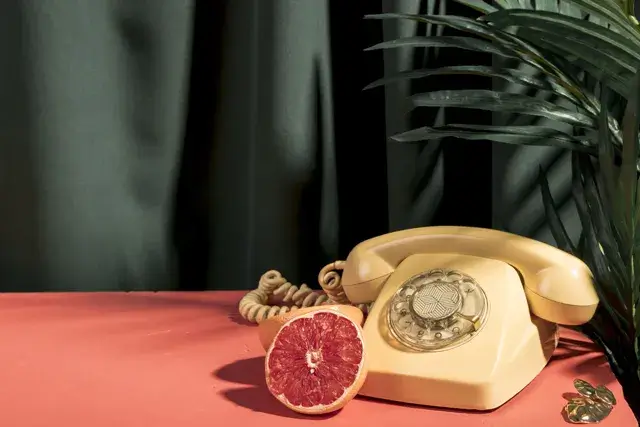 On the table, there is a yellow telephone next to a grapefruit