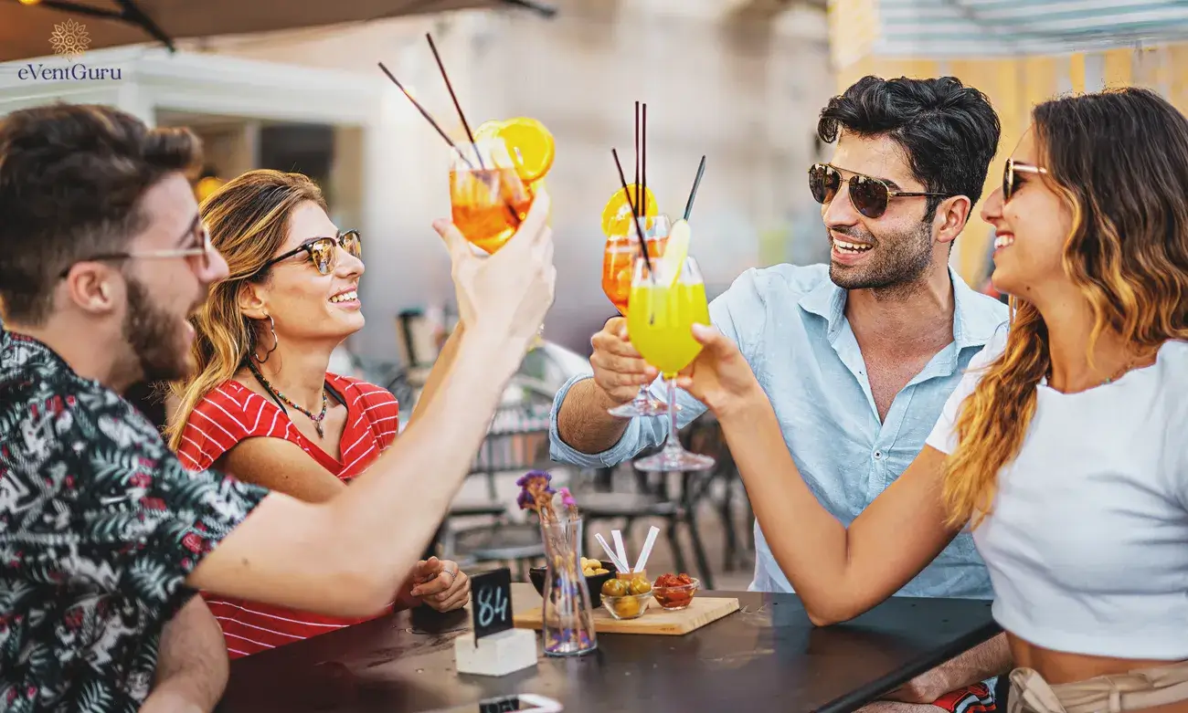 Young vacationers sit carefree at a pub restaurant with an alcohol-lifestyle concept, toasting fresh cocktail glasses at a summer outdoor pub restaurant