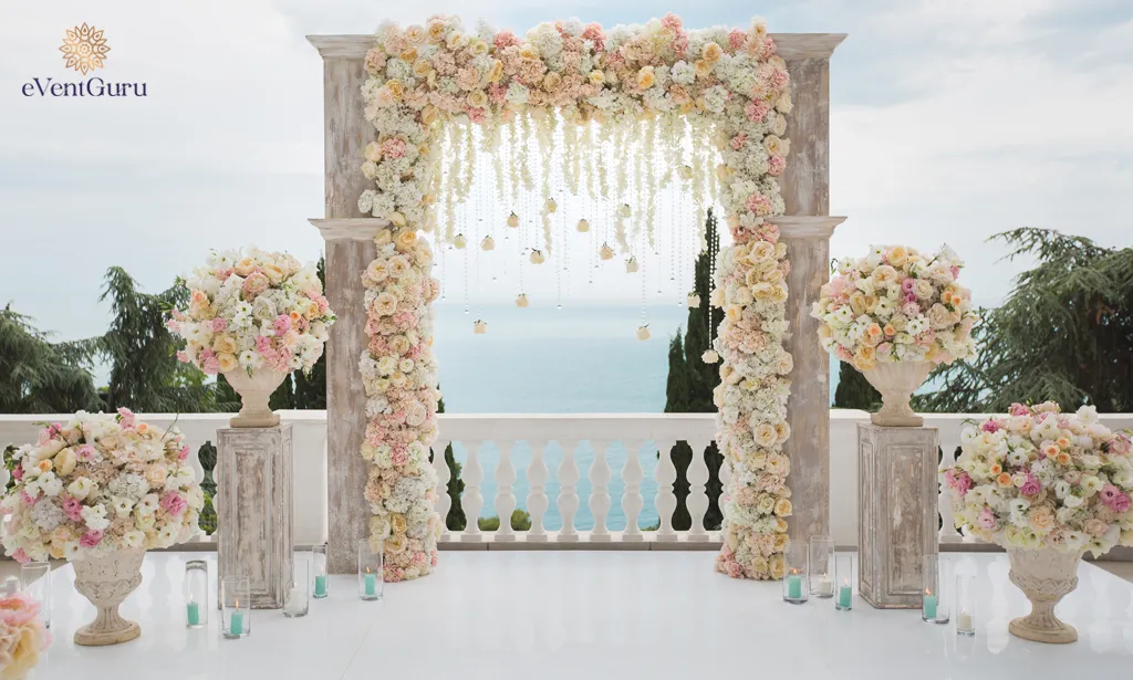 Fresh flowers, vases on the ocean, and blue skies enhance this elegant wedding arch