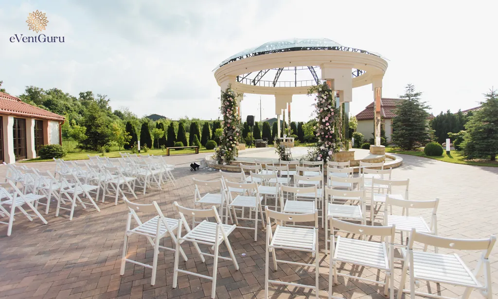 An outdoor view of white guest chairs and a decorated ceremonial archway on a sunny day